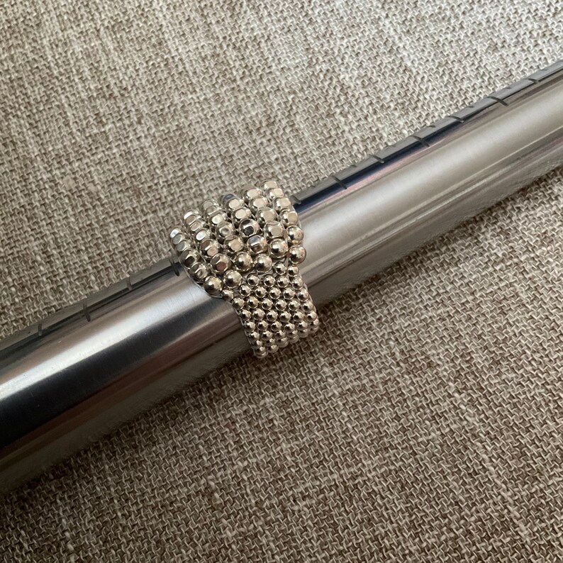 May include: A silver beaded ring with a textured surface. The ring is made of small, round beads that are tightly packed together.