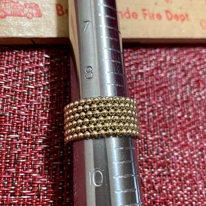 May include: A gold ring with a beaded design, measured on a ring sizer that shows a size 8.
