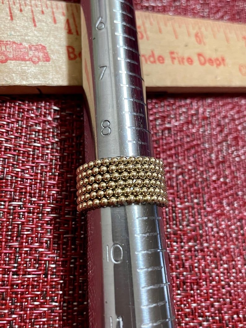May include: A gold ring with a beaded design, measured on a ring sizer that shows a size 8.