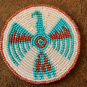 May include: A round beaded design with a turquoise and orange pattern. The design is of a stylized bird with a circular pattern in the center.