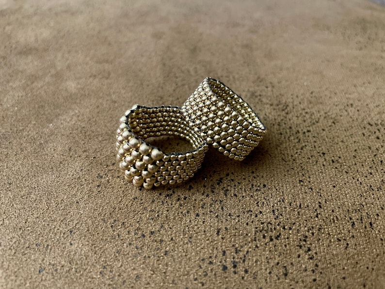 May include: Two gold-toned rings made of small, round beads. The rings are stacked on top of each other.