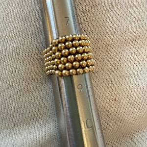 May include: A gold ring made of small beads, measured on a metal ring sizer with markings for sizes 6, 7, 8, 9, 10, and 11.