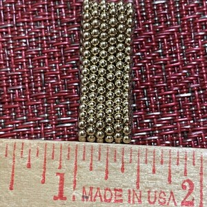 May include: A close-up of a ruler with the words "Made in USA" printed on it. A small, rectangular block of gold-coloured magnetic balls is sitting on top of the ruler. The block is approximately 2.5 cm long.
