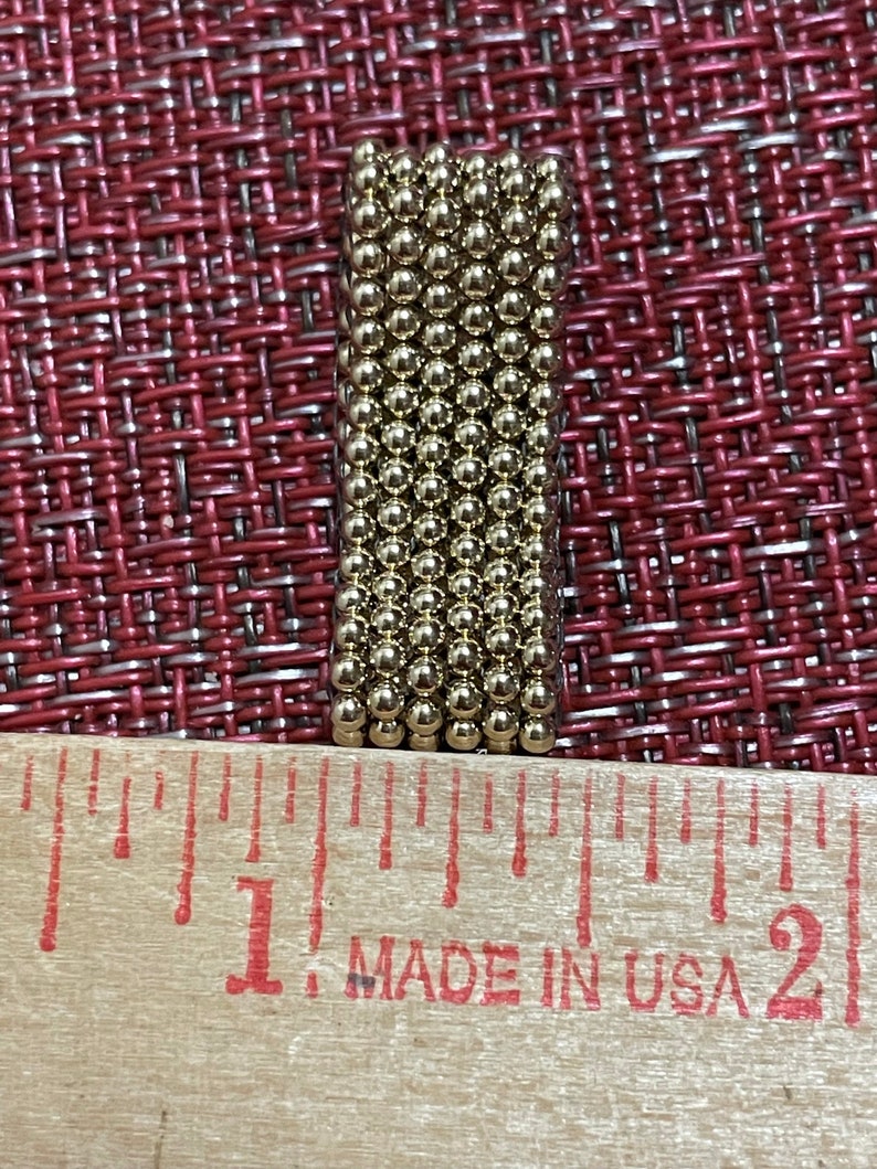May include: A close-up of a ruler with the words "Made in USA" printed on it. A small, rectangular block of gold-coloured magnetic balls is sitting on top of the ruler. The block is approximately 2.5 cm long.