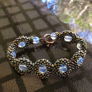 May include: A beaded bracelet with a copper clasp and iridescent blue glass beads. The bracelet is made with dark gray and copper seed beads.
