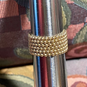May include: A gold ring made of small beads, stacked on top of each other. The ring is on a silver metal surface.