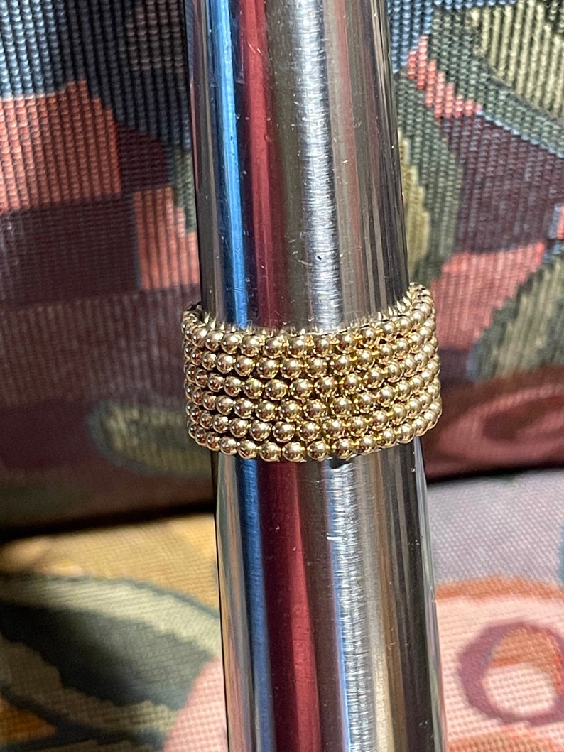 May include: A gold ring made of small beads, stacked on top of each other. The ring is on a silver metal surface.
