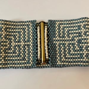 May include: A blue and white beaded bracelet with a gold metal clasp. The bracelet is made of small, round beads that are arranged in a geometric pattern.