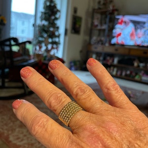 May include: A gold beaded ring with multiple rows of beads. The ring is worn on a hand with pink glitter nail polish.