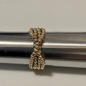 May include: A gold beaded ring with a woven design. The ring is made of small, round beads that are tightly woven together to create a unique and stylish look.