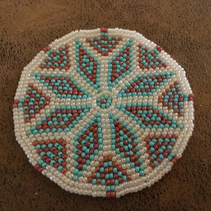 May include: A round beaded coaster with a geometric pattern in shades of white, turquoise, and orange.