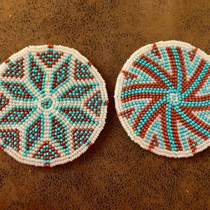 Puede incluir: Dos posavasos redondos de cuentas con fondo blanco y patrones geométricos en turquesa y marrón.
