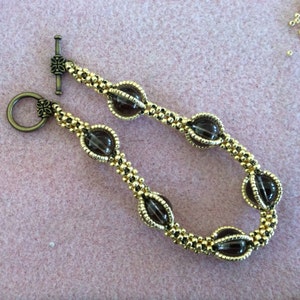 May include: A gold beaded bracelet with a brown oval-shaped bead at each end. The bracelet has a toggle clasp.