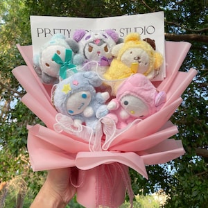 May include: A pink bouquet of plush toys with a white card that says "PRETTY THINGS STUDIO". The bouquet includes a blue, yellow, pink, and purple plush toy.