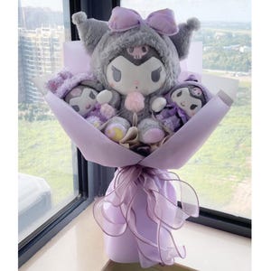 May include: A bouquet of plush toys wrapped in purple paper. The bouquet features a large grey and purple plush toy with a skull and crossbones design, and two smaller plush toys with purple and black accents.