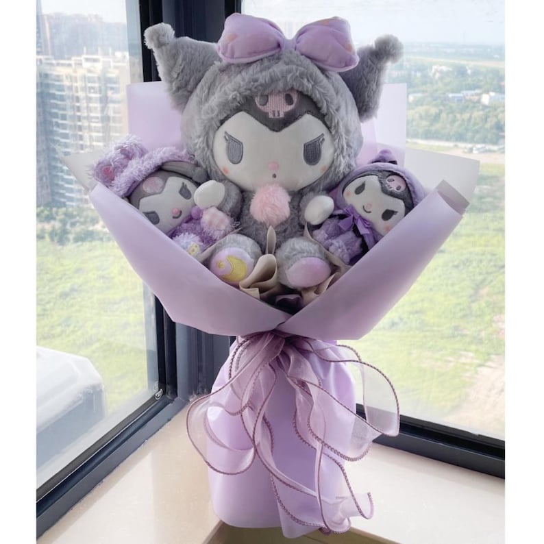 May include: A bouquet of plush toys wrapped in purple paper. The bouquet features a large grey and purple plush toy with a skull and crossbones design, and two smaller plush toys with purple and black accents.