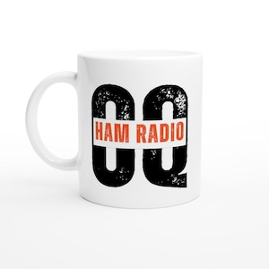 Op de afbeelding: Witte keramische mok met een zwart grafisch ontwerp en de woorden "HAM RADIO" in oranje. De mok heeft een gebogen handvat en is geschikt voor warme of koude dranken.