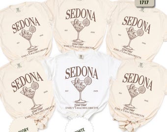 May include: Several ivory and white t-shirts with the word "SEDONA" in a brown font. Each shirt features a cocktail glass design with the text "Girls Club" and "Emily's Bachelorette". The shirts are for a bachelorette party.