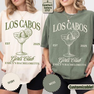 May include: Ivory and moss green t-shirts with the text "LOS CABOS" above a margarita glass graphic. Below the graphic is "Girls Club" and "EMILY'S BACHELORETTE". The shirts also have the text "EST 2025".