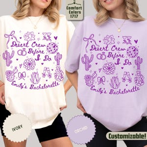May include: Two t-shirts, one ivory and one orchid, featuring a purple graphic design. The design includes text that reads "Desert Crew Before I Do" and "Emily's Bachelorette", along with cacti, hearts, and other decorative elements. The shirts are customizable.
