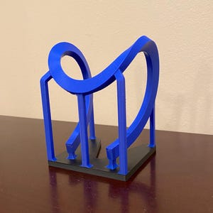 Puede incluir: Una escultura azul impresa en 3D con un diseño en bucle. La escultura tiene una base negra y está sobre un fondo neutro. El diseño presenta una forma continua y fluida.