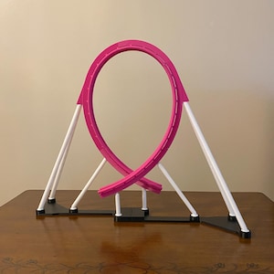 May include: A pink roller coaster toy with a loop-de-loop design. The track is supported by white and black structures, creating a miniature amusement park ride. The toy is designed for play and display.