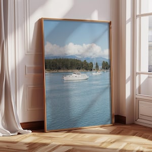 May include: A framed print featuring a serene coastal scene. The image showcases a calm blue body of water with several boats, including a white motorboat. In the background, there are mountains and a forest under a partly cloudy sky.