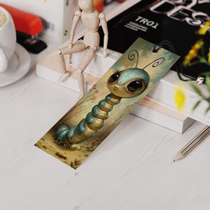 May include: A whimsical bookmark featuring a cartoon caterpillar with large, expressive eyes. The caterpillar is primarily blue and gold, set against a soft, illustrated background. The bookmark is rectangular with a small hole at the top.