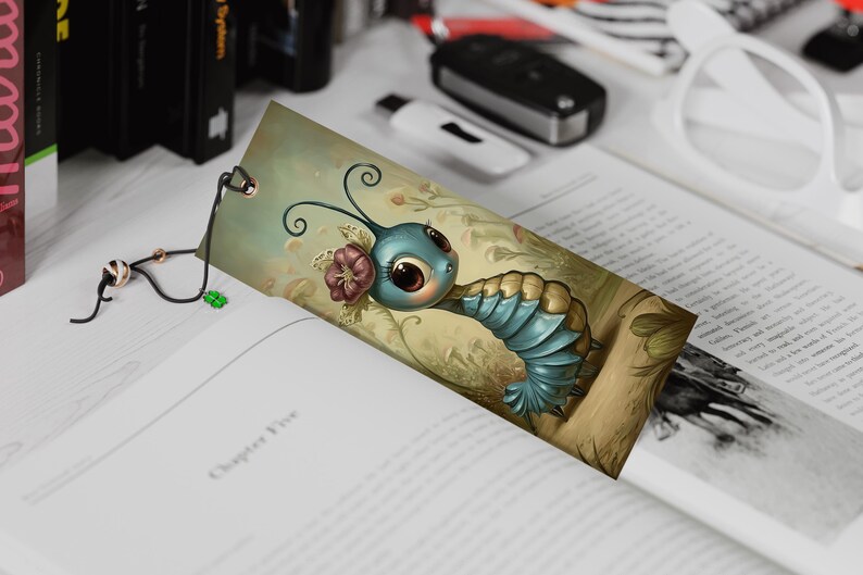 May include: A whimsical bookmark featuring a cartoon caterpillar with large eyes, blue segmented body, and a flower. The bookmark is inserted into a book, with a black and gold cord attached.