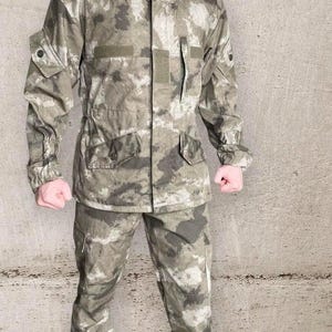 May include: A camouflage jacket and pants set in shades of green, gray, and brown. The jacket has a hood, multiple pockets, and a button-up front. The pants have a matching camouflage pattern. The outfit is designed for outdoor activities.
