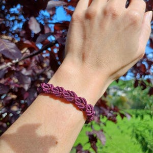 Könnte beinhalten: Ein Nahaufnahme eines geflochtenen Armbands in Marsala auf einem Handgelenk. Das Armband besteht aus einem dicken Band und hat ein schlichtes, elegantes Design.