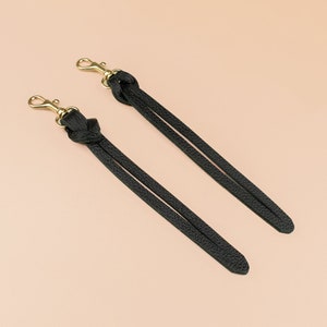May include: Two black leather straps with gold clasps. The straps are knotted at the top and have a braided texture.