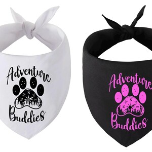 May include: Two dog bandanas, one white with black paw print and text "Adventure Buddies", the other black with pink paw print and text "Adventure Buddies".
