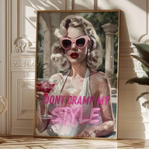 May include: A framed print featuring a woman with blonde hair, wearing pink sunglasses and holding a cocktail. The print has the text "DON'T CRAMP MY STYLE" in pink. The artwork is displayed in a room with a white sofa and a plant.