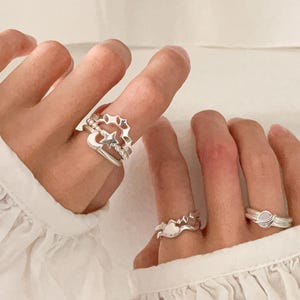 Könnte beinhalten: Silberringe mit Himmelsmotiven, darunter Sterne, Monde und Planeten. Die Ringe werden an Fingern getragen und zeigen ihre komplizierten Details und ihre filigrane Verarbeitung. Die Ringe bestehen aus einem glänzenden, metallischen Material.