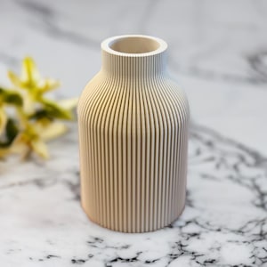 May include: A white ceramic vase with a ribbed design. The vase is a simple, modern design and would look great in any home.