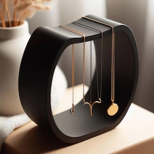May include: A black, modern jewelry display stand with a curved, open design. Several gold necklaces hang from the top, showcasing various pendant styles. The stand is made of a matte black material, creating a sleek and minimalist aesthetic.