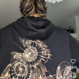 May include: Black hoodie with a large, intricate bleach design on the back. The design features a floral or mandala-like pattern in a lighter color, creating a striking contrast. The text "bleach tutorial !!!" is visible at the bottom.