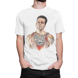 May include: White t-shirt featuring a detailed illustration of a man with a cigarette, tattoos, and a blood-stained undershirt. The graphic includes a skull and the text "Yippee Ki Yay Motherfucker".