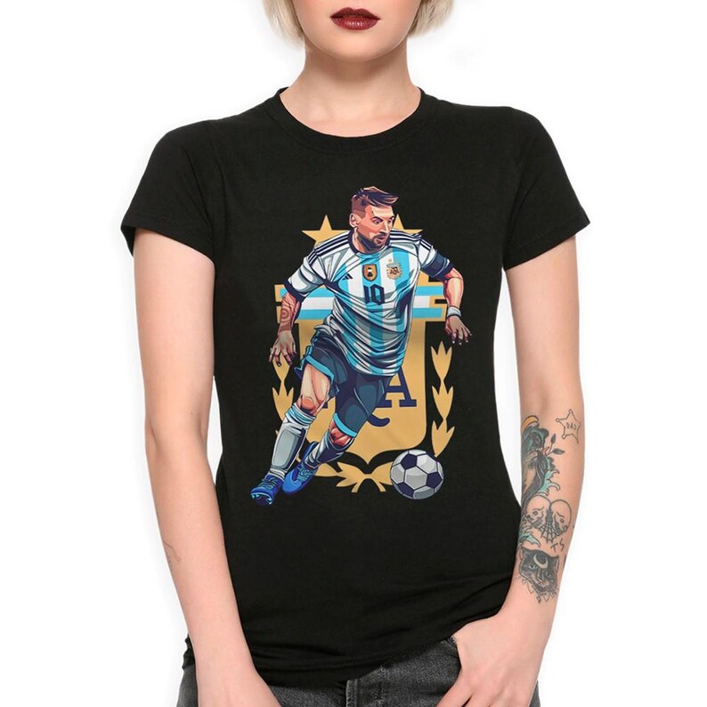 May include: Black t-shirt with a graphic of a soccer player wearing a blue and white jersey with the number 10 on it. The player is dribbling a soccer ball and is surrounded by a gold crest with the letters "AFA".