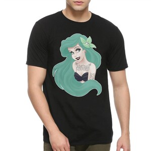 Puede incluir: Camiseta negra con un estampado gr&aacute;fico de una sirena de pelo verde con tatuajes y el texto "Lost at Sea".
