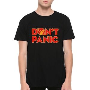 Puede incluir: Camiseta negra con texto rojo que dice "DON'T PANIC" con un gráfico amarillo y rojo de un planeta y un puño.