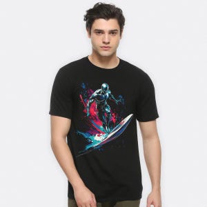 May include: Black t-shirt with a surfing graphic. The design shows a silver figure surfing on a blue and white surfboard, set against a backdrop of red, blue, and purple splashes.