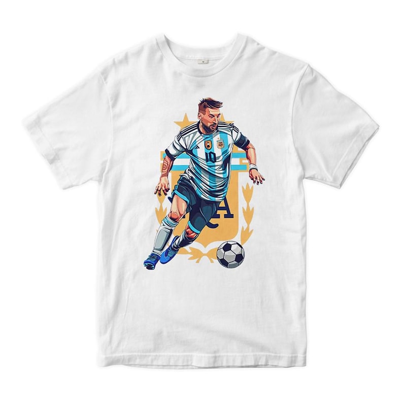 May include: White t-shirt with a graphic of a soccer player in a blue and white jersey, dribbling a soccer ball. The player is wearing a blue headband and has a determined expression on his face. The graphic is surrounded by a gold crest with the letters "A" and "F" visible.