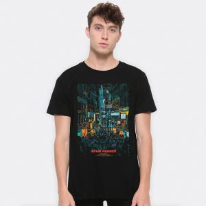 以下が含まれることがあります： 未来都市の街並みをグラフィックプリントした黒いTシャツ。"ブレードランナー"の文字が入っています。