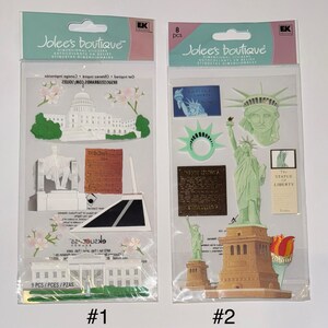 May include: Two packages of dimensional stickers featuring American landmarks. The first package has a sticker of the Capitol Building, the Washington Monument, and the White House. The second package has stickers of the Statue of Liberty, the torch, and the Liberty Bell. Both packages have the text "Jolee's Boutique" and "Dimensional Stickers".