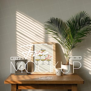 May include: A framed print with a champagne tower illustration, a vintage clock, and a potted plant on a wooden table. The print features the text "Fête Vita" in red script. The scene is lit by sunlight from a window.
