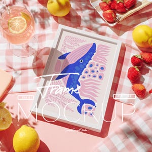 May include: A white framed art print featuring a blue whale illustration with pink accents. The artwork is set on a pink and white checkered surface, surrounded by lemons, strawberries, and a glass of pink drink with a lemon slice.