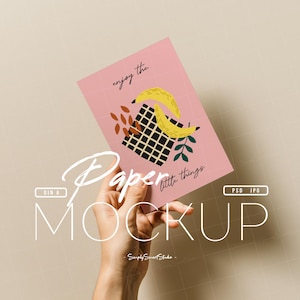 Könnte beinhalten: Ein rosa Papier-Mockup, das von einer Hand gehalten wird, mit einem Design aus gelben Bananen, einem schwarz-weiß karierten Quadrat und dem Text "enjoy the little things". Das Mockup enthält auch den Text "Paper Mockup".