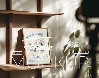 May include: A framed poster mockup with the words "Pasta & Wine Lover Club" in blue and white. The poster is on a wooden shelf, with the word "MOCKUP" in large white letters. The image includes a plant and shadows.